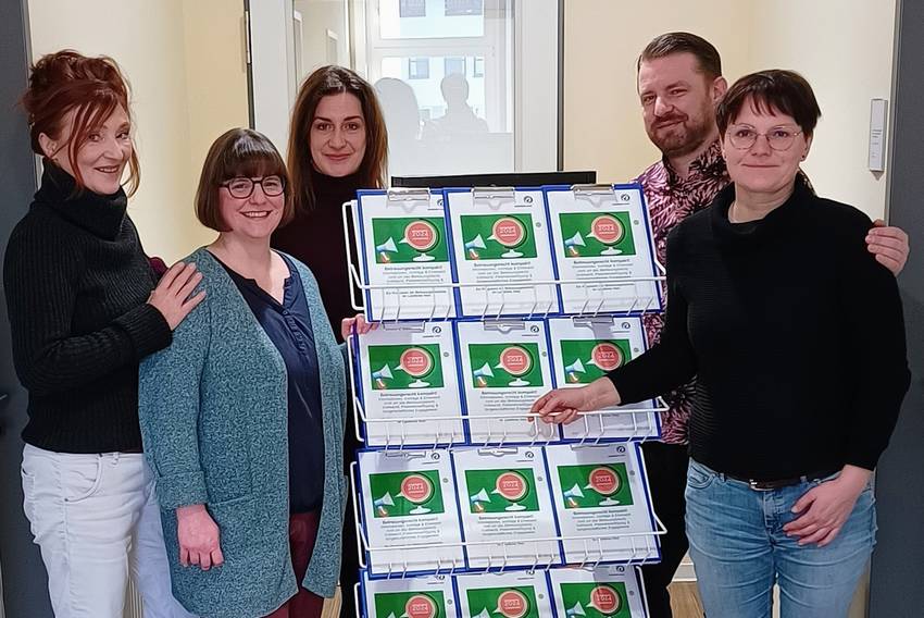 Fünf Menschen stehen in einem Raum und zeigen ein Schulungsprogramm Fünf Menschen stehen in einem Raum und zeigen ein Schulungsprogramm