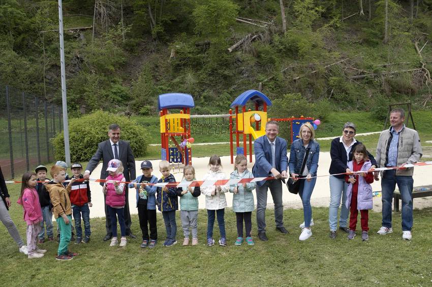 Erwachsene und Kinder auf einem neuen Spielplatz, die ein Band durchschneiden Erwachsene und Kinder auf einem neuen Spielplatz, die ein Band durchschneiden
