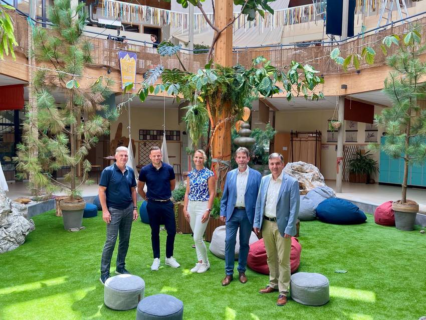 Das Foto zeigt mehrere Personen, die auf einem Rasen stehen und von einzelnen Kiefern umgeben sind. Das Foto zeigt mehrere Personen, die auf einem Rasen stehen und von einzelnen Kiefern umgeben sind.