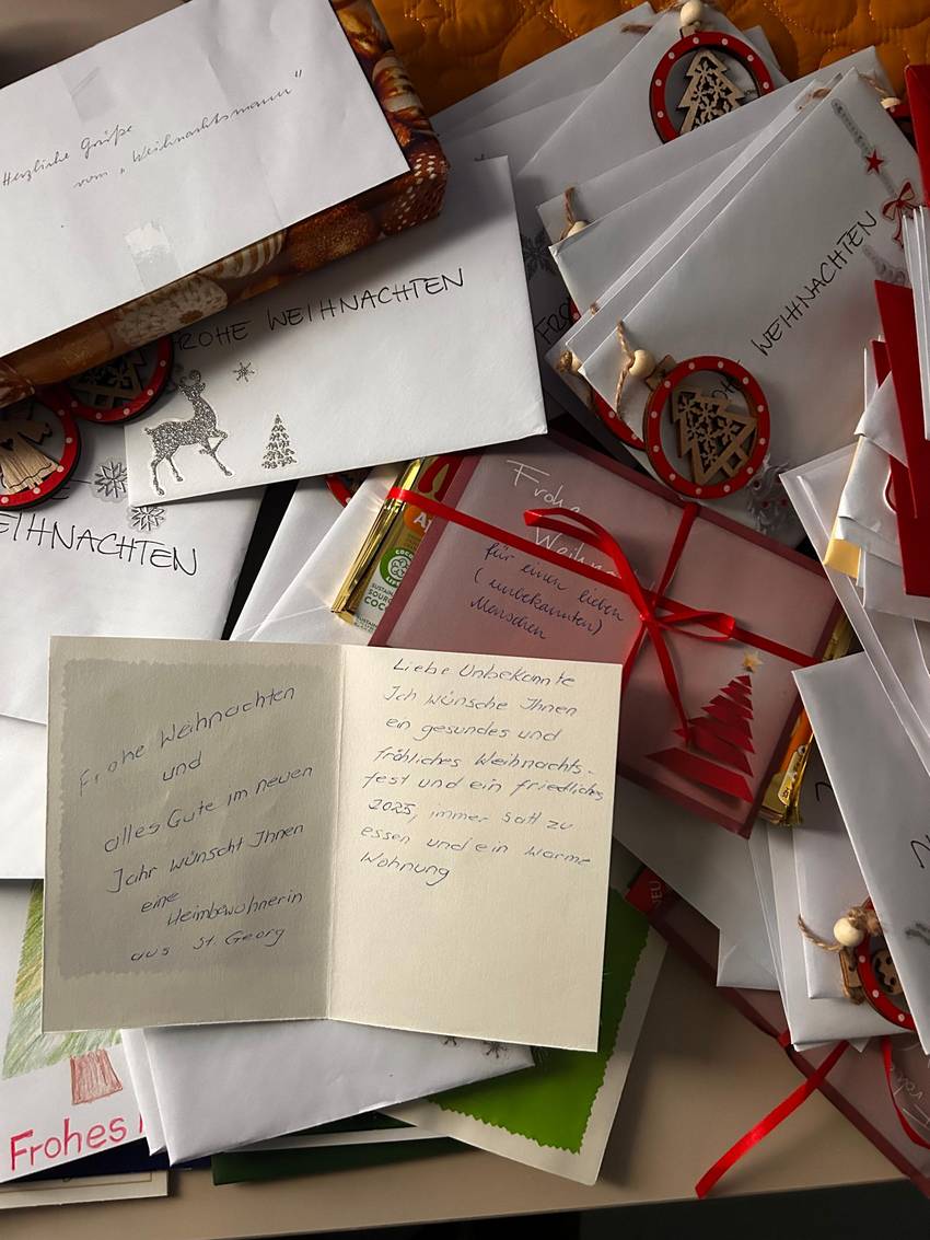 Viele Weihnachtskarten auf einem Haufen, oben drauf ist eine Karte aufgeklappt, die handschriftlich beschrieben ist. Viele Weihnachtskarten auf einem Haufen, oben drauf ist eine Karte aufgeklappt, die handschriftlich beschrieben ist.