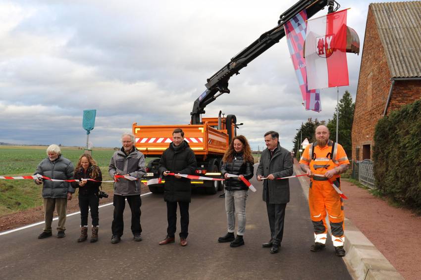 Mehrere Personen stehen auf einer Straße und schneiden ein Absperrband durch, weil eine Straße wieder freigegeben ist. Im Hintergrund steht ein Baufahrzeug. Mehrere Personen stehen auf einer Straße und schneiden ein Absperrband durch, weil eine Straße wieder freigegeben ist. Im Hintergrund steht ein Baufahrzeug.