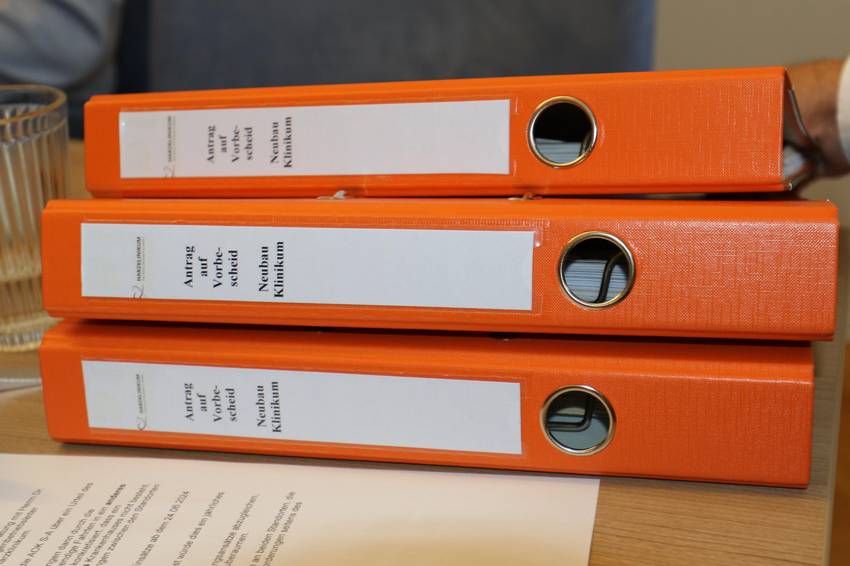 Drei Ordner mit der Aufschrift "Antrag auf Vorbescheid Neubau Klinikum", die auf einem Tisch liegen