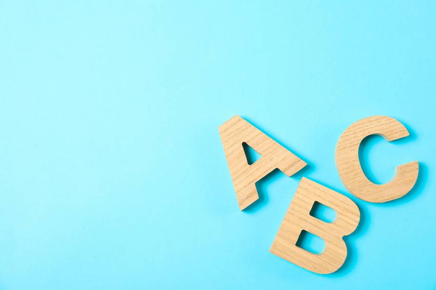 Die Buchstaben A B und C aus Holz auf blauem Hintergrund.