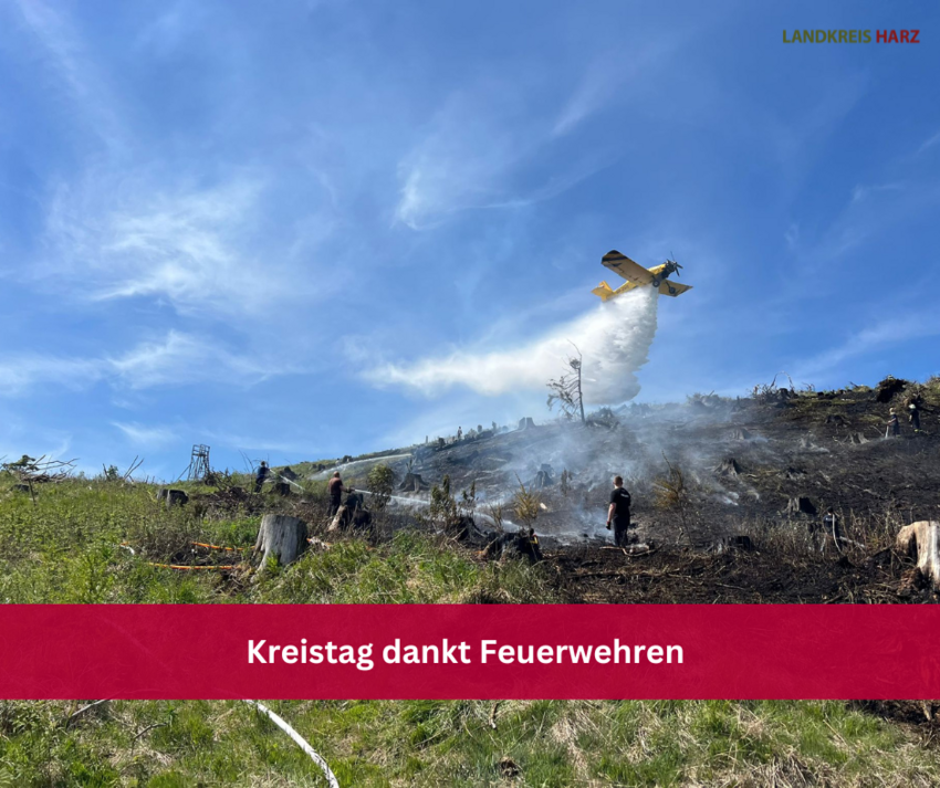 Das Löschflugzeug Hexe 1 des Landkreises Harz beim Löschvorgang über einem abgebrannten Waldstück. Auf dem Bild ist ein roter Balken mit der Aufschrift Kreistag dankt Feuerwehren.