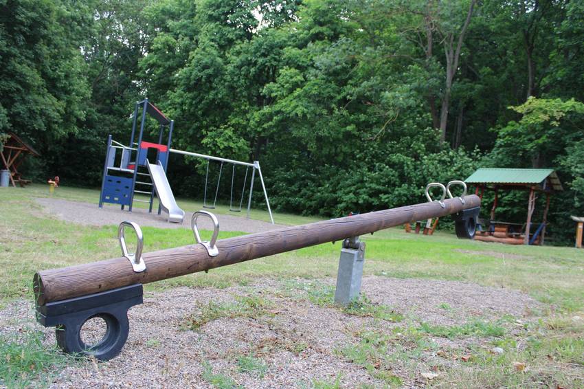 Ein Spielplatz. Im Vordergrund steht eine Wippe, im Hintergrund ein Kletterturm mit Rutsche. Ein Spielplatz. Im Vordergrund steht eine Wippe, im Hintergrund ein Kletterturm mit Rutsche.