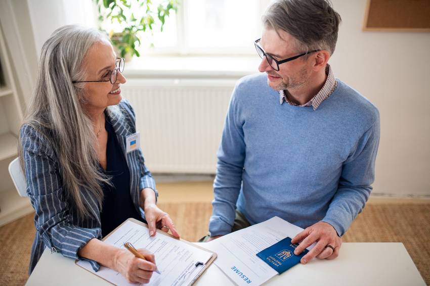 Eine Frau und ein Mann, die sich unterhalten. Auf dem Tisch vor IHnen liegen Unterlagen.