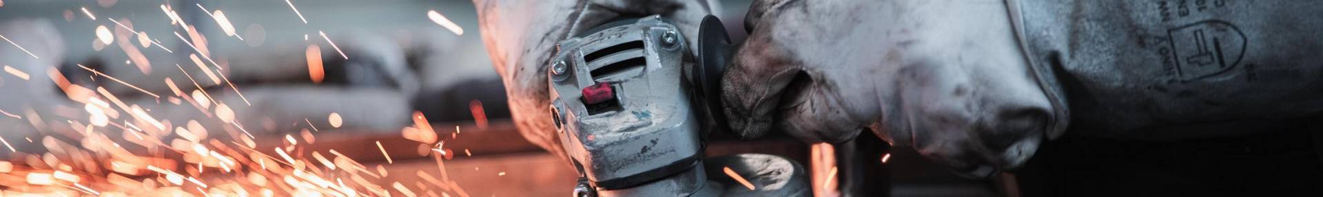 Hände in Arbeitshandschuhen, die ein Schleifgerät halten, Funkenflug am Metall, das geschliffen wird.
