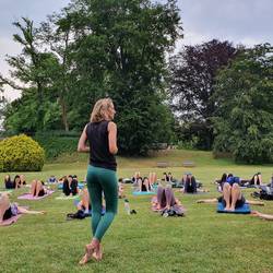 Menschen beim Yoga, Lehrerin steht vorne und mehrere Menschen in Yogaposen im Freien