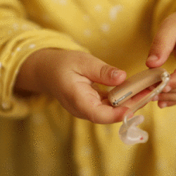 Auf dem Bild ist eine Person, die ein Hörgerät in der Hand hält.