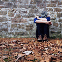 Auf dem Bild ist ein Junge der alleine vor einer Mauer sitzt.
