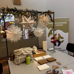 Auf dem Bild ist ein Basteltisch mit Bastelutensilien wie Scheeren, Papier und Glitzer. Im Hintergrund sind Sterne und Lichterkette und das Banner vom Örtlichen Teilhabemanagement.