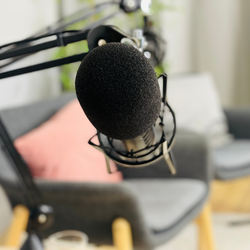 Symbolbild Podcast - Ein Mikrofon im Vorgrund, zwei Stühle verschwommen im Hintergrund.
