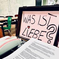 Projekttag "Was ist Liebe" Auf dem Bild ist ein Koffer der aufgeklappt ist und darin ist ein Schriftzug "Was ist Liebe?"
