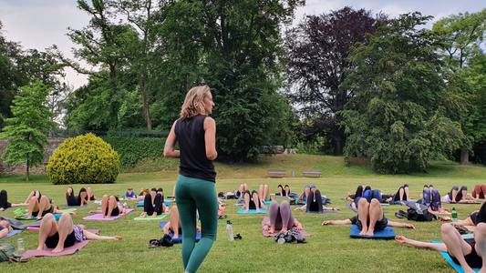 Yogakurs im Lustgarten in Wernigerode Menschen beim Yoga, Lehrerin steht vorne und mehrere Menschen in Yogaposen im Freien