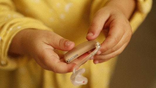 Auf dem Bild ist eine Person, die ein Hörgerät in der Hand hält.