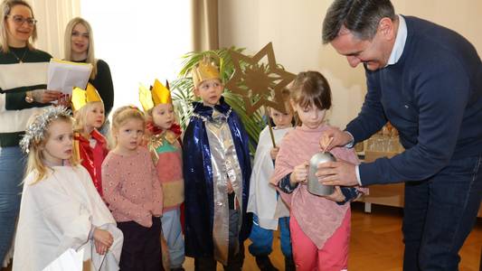 Das Bild zeigt den Landrat, wie er den Sternensingern, die vor ihm stehen, Geld in die Spendenspardose steckt.