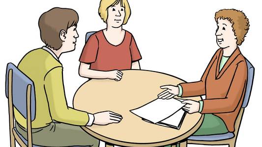 Drei Menschen sitzen an einem Tisch, einer ist der Berater und zwei Menschen hören ihm zu.