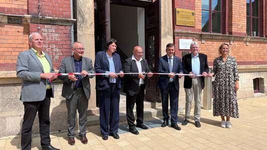 Das Bild zeigt mehrere Personen, die ein Band durchschneiden. Sie stehen vor der neu sanierten Bosse Sekundarschule.
