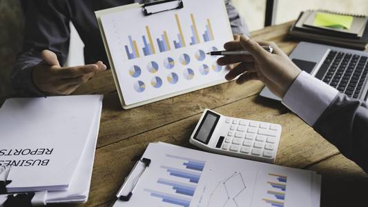 Auf einem Tisch sind Abbildungen von Diagrammen. Eine Hand zeigt auf diese Diagramme.