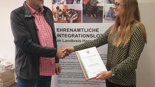 Susanne Reinhardt von der Koordinierungsstelle für Migration und Ehrenamt übereicht Klaus Mansfeldt seine Ernennungsurkunde.