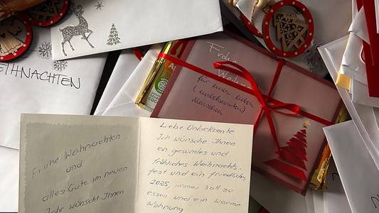Viele Weihnachtskarten auf einem Haufen, oben drauf ist eine Karte aufgeklappt, die handschriftlich beschrieben ist.