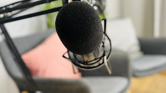 Symbolbild Podcast - Ein Mikrofon im Vorgrund, zwei Stühle verschwommen im Hintergrund.