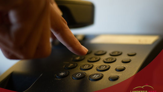 Eine Hand, die einen Telefonhörer in der hält und eine zweite, die Zahlen auf dem Tastenfeld drückt. Unten ein roter Bereich mit der Aufschrift Veränderte Sprechzeiten des Sozialpsychiatrischer Dienst beim Landkreis Harz.
