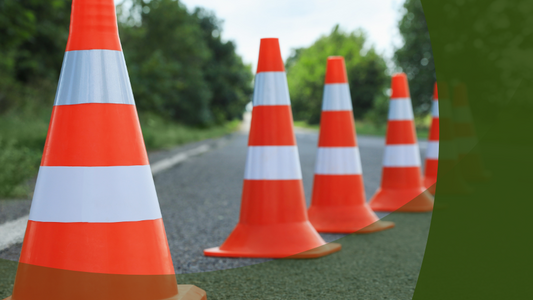 Symbolbild Straßensperrung - Absperrpylonen auf einer Straße - rechts ist ein grüber Bereich, unten auch. Im unteren Teil steht Sperrung der Kreisstraße 1329  zwischen Ortsausgang Minsleben und L 82 ab 18. Mai.