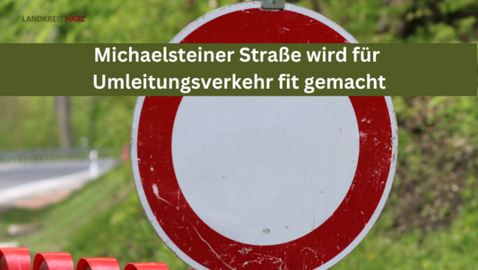 Durchfahrt-verboten-Schild auf einer Absperrbake. Auf dem Bild ist ein grüner Balken mit der Aufschrift Michaelsteiner Straße wird für Umleitungsverkehr fit gemacht.