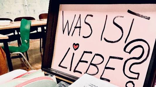 Auf dem Bild ist ein Koffer der aufgeklappt ist und darin ist ein Schriftzug "Was ist Liebe?"